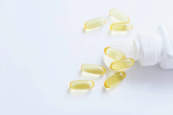 Витаминные капсулы с рыбьим маслом, выходящие из пузырька с таблетками на белом фоне — стоковое фото