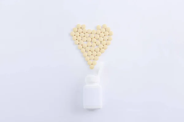 Фармацевтические лекарства таблетки разлива из бутылки с таблетками в форме сердца на белом фоне, вид сверху — стоковое фото