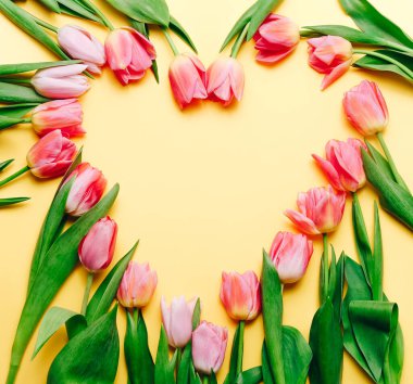 Many pink tulips in shape of heart on a beige background. Top view