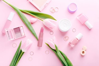 Makyaj için kozmetik ürünler ve pembe arka planda pembe laleler ile düz konum