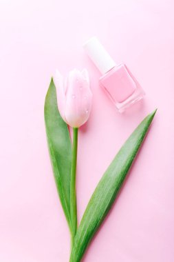 Pink nail polish bottle with beautiful tulip on pink background