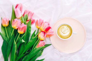 Delicious coffee and a bouquet of pink tulips in a bed