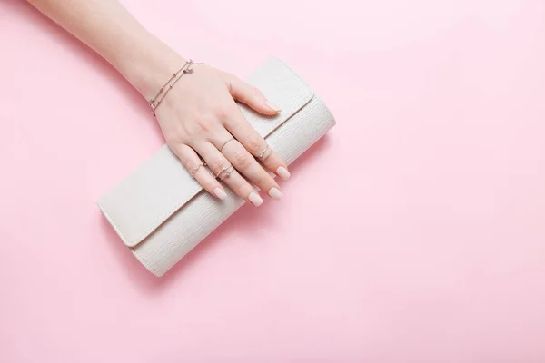 Female hand with jewelry and clutch bag on pink background