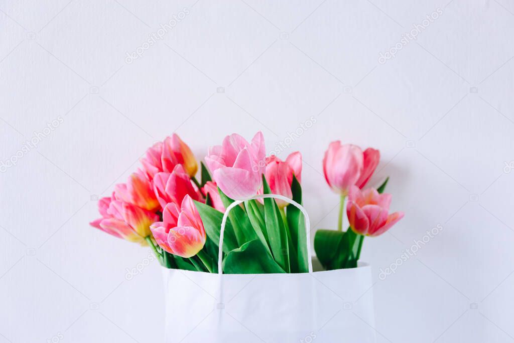 Fresh pink tulip flowers in paper bag on white background