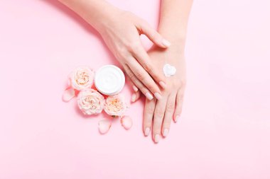 Womans hands with natural cream. Care about soft, smooth skin. Beautiful fresh roses on pink table.