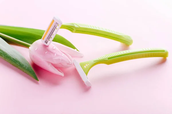 Green razor with beautiful pink tulip on a pink background. Hair removal concept. — Stock Photo, Image