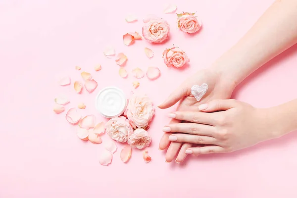 Mujeres manos con forma de corazón creado a partir de crema natural. Cuida la piel suave y lisa. Hermosas rosas frescas en la mesa rosa . — Foto de Stock