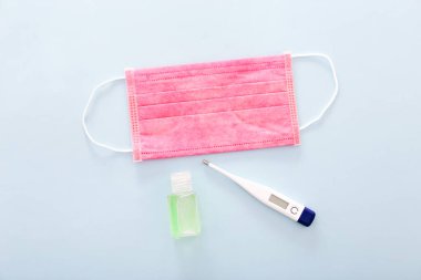 Tıbbi maske, termometresi olan tıbbi koruyucu maske ve mavi arka planda el dezenfektanı. Sağlık ve Tıp Konsepti.