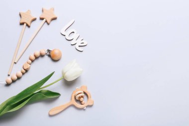 Gri arka planda beyaz laleleri olan bebek oyuncakları ve aksesuarları. Yeni doğan şeyleri. Düz yatış, üst görünüm