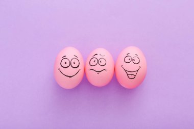 Mor arka planda yüzü olan komik pembe yumurtalar.