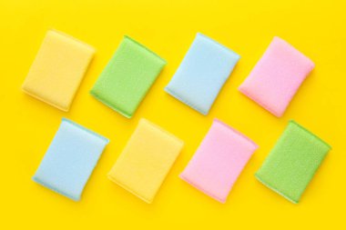 Mutfakta sarı arka planda farklı yüzeyler için renkli temizlik süngerleri. Üst manzara, düz uzanma