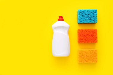 Mutfakta sarı arka planda farklı yüzeyler için renkli temizlik seti. Üst manzara, düz uzanma