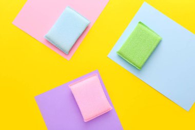 Mutfakta sarı arka planda farklı yüzeyler için renkli temizlik süngerleri. Üst manzara, düz uzanma