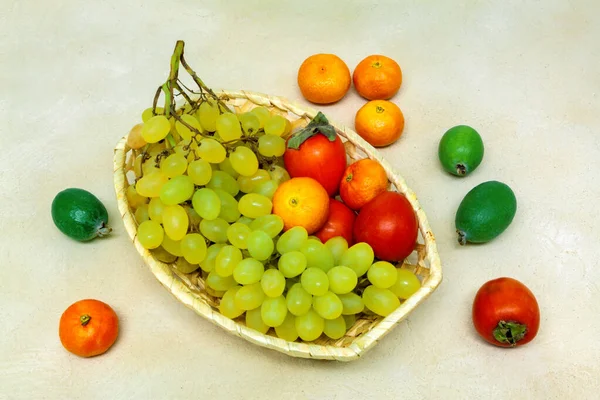 Korb mit hellen Trauben und reifen Früchten auf grauem Hintergrund — Stockfoto