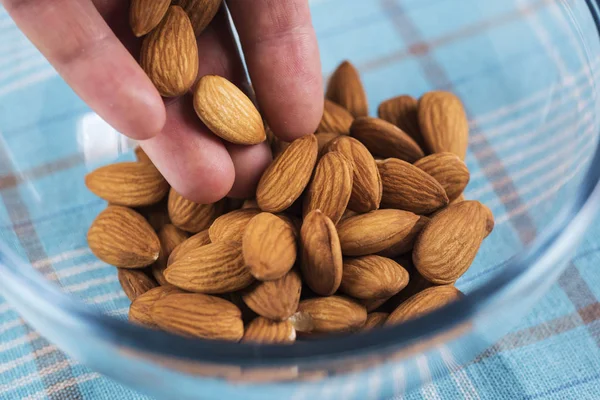 Almonds fall from palm of your hand into a glass bowl on the table.