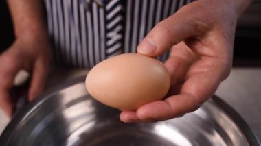 Eller ve metal çelik bıçak kahverengi bir tavuk yumurtasını kırar ve yumurta sarısı metal bir tavaya düşer. Yakın plan..
