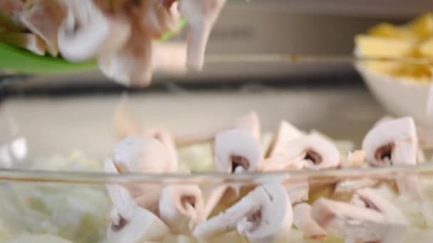As mãos femininas lançam champinhons fatiados com uma faca de uma tábua de corte em uma tigela . — Vídeo de Stock