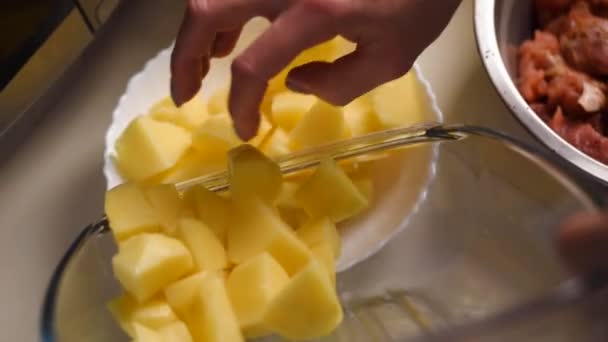 Close up como um homem coloca batatas picadas em uma tigela amarela de uma tábua de cortar — Vídeo de Stock