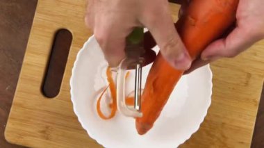 Erkek eli taze havucu doğrama tahtasının üzerine soyar. Yaklaş, üst manzara..