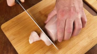 Bıçaklı adamın elleri kesme tahtasındaki ince tavuk filetosu..