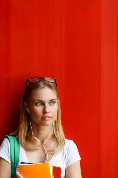 Студент з навушниками на фоні порожньої червоної стіни — стокове фото