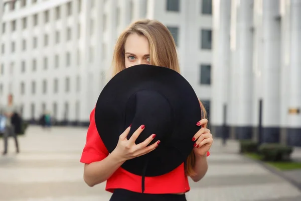 Foto-Blondine in roter Jacke verdeckt Gesicht mit schwarzem Hut — Stockfoto