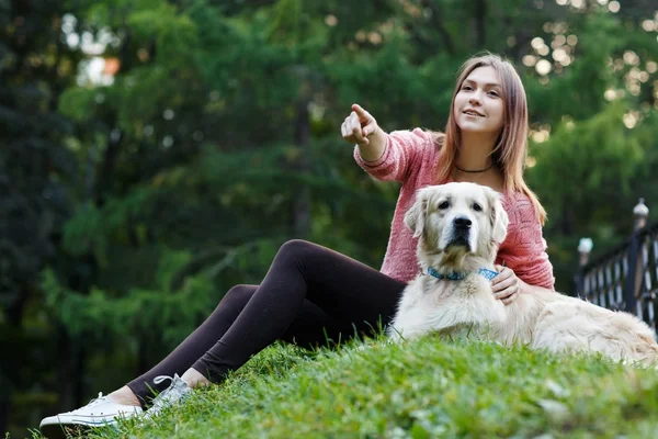 Foto de baixo da mulher apontando para a frente ao lado do cão no gramado verde — Fotografia de Stock