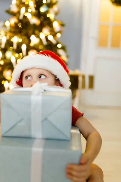 Foto de Año Nuevo de niño en gorra de Santas con caja de regalo en el fondo —  Fotos de Stock
