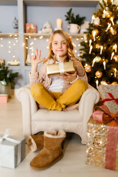 Imagen de niña sentada en silla sobre fondo de decoraciones navideñas — Foto de Stock