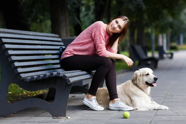 レトリーバー犬のベンチに座って微笑んでいる女の子の画像 — ストック写真