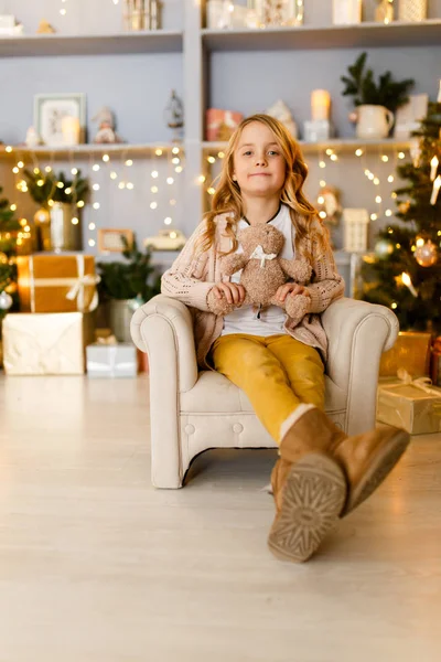 Foto de niña sentada en silla en el fondo de las decoraciones de Navidad — Foto de Stock