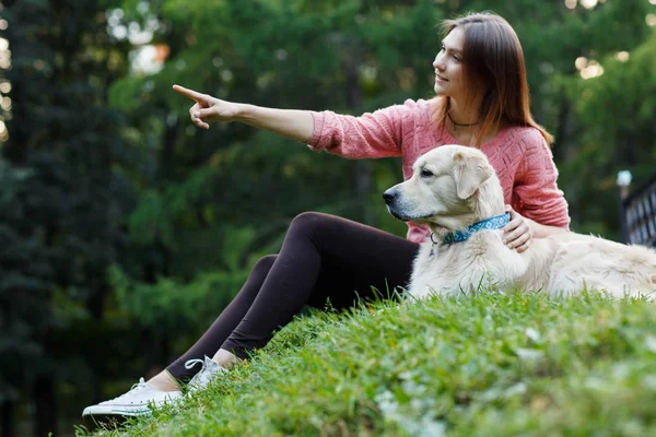 Изображение снизу девушки, указывающей вперед рядом с собакой на зеленой лужайке — стоковое фото