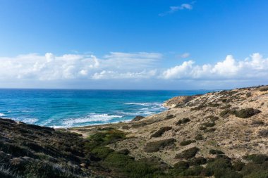 Deniz, bulutlu gökyüzü ve tepelik yamaç fotoğrafı