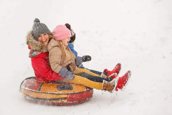 Bilden av mamma med sin dotter och son Rider slangar i snöfall — Stockfoto