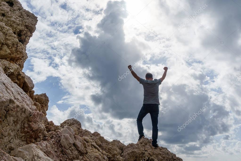 Photo from back of man with hands up on mountain