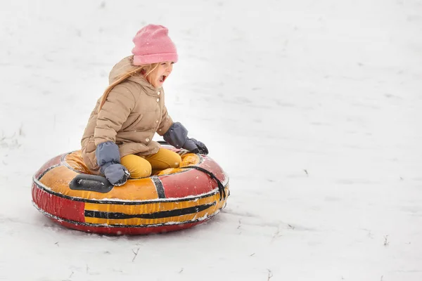 Picture of happy little girl wearing pink cap riding on tubing — Stock Photo, Image