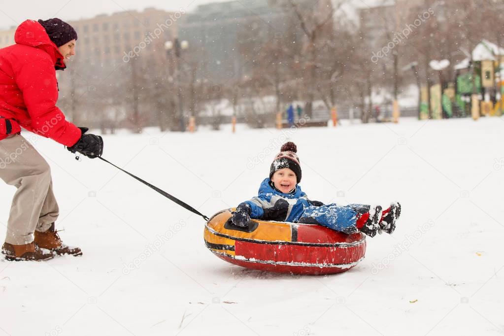 Picture of cheerful father skating son on tubing in winter afternoon