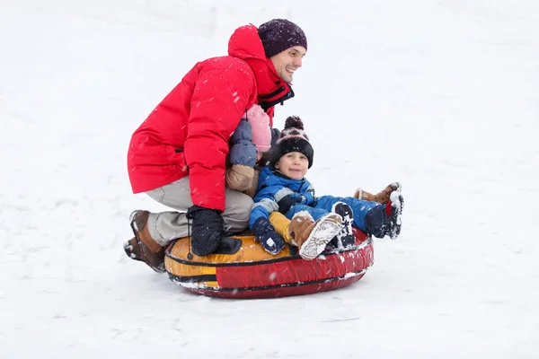 Фото отца, сына, дочерей, катающихся на трубах в зимнем парке — стоковое фото