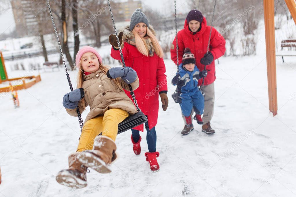 Picture of girl and boy swinging in winter in park with parents