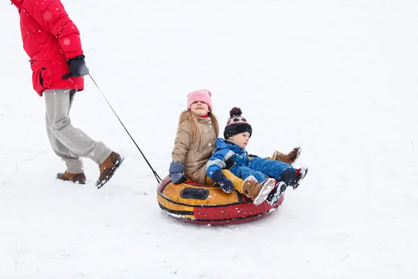 Photo of father skating son and daughter on tubing in winter park — Stock Photo, Image