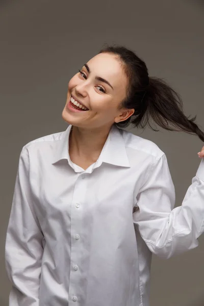 Krásná dívka v bílé košili ukazuje emoce - úsměv, zábava. Na světlém pozadí. — Stock fotografie