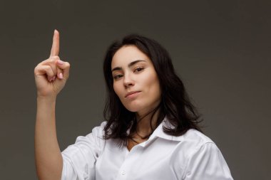 Beautiful girl in a white shirt with a raised finger up. On a light background. clipart