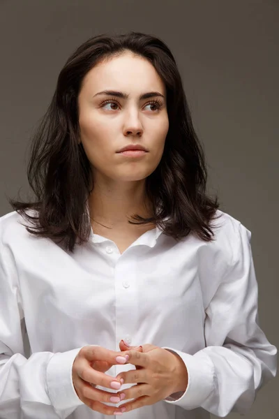 Hermosa chica en una camisa blanca muestra emociones - reflexividad. Sobre un fondo claro . — Foto de Stock