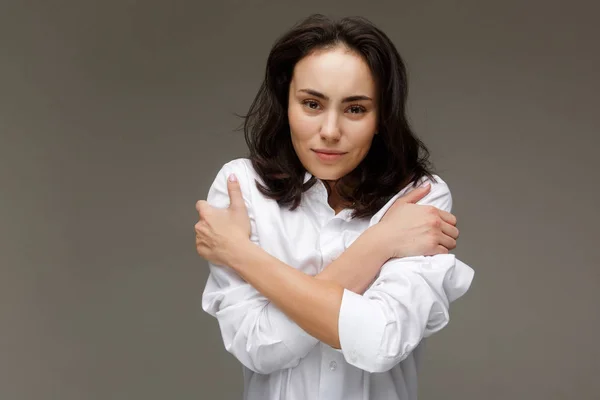 Hermosa chica con una camisa blanca se abraza. Sobre un fondo claro . — Foto de Stock