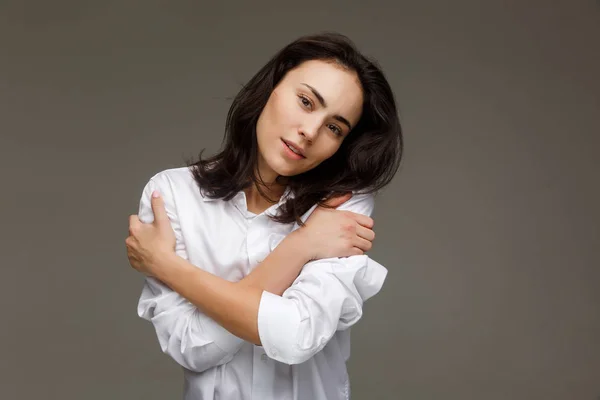 Hermosa chica con una camisa blanca se abraza. Sobre un fondo claro . —  Fotos de Stock