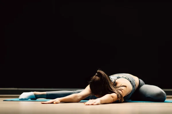 Atletisch meisje stretching liggend op tapijt in sporthal — Stockfoto