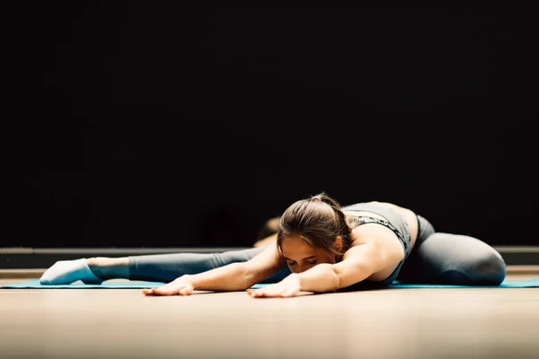 Atletische vrouw stretching liggend op tapijt in sporthal — Stockfoto