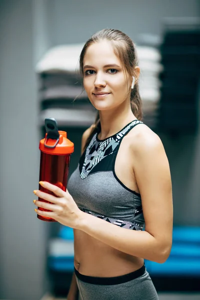 Спортивная женщина с красной бутылкой воды на размытом фоне — стоковое фото