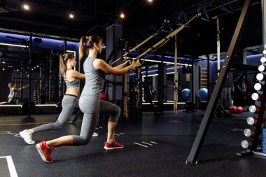 İki sporcu kadın, spor salonunda elastik bantlarla trenler kaldırıldı.