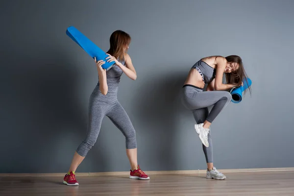 Deportivas mujeres luchando contra alfombras azules retorcidas contra la pared gris vacía — Foto de Stock